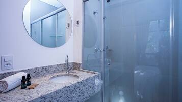 A bathroom with a granite countertop sink, a round mirror, and a glass-enclosed shower.