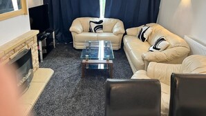 Un soggiorno con due divani beige, un tavolino in vetro, un camino e una televisione.