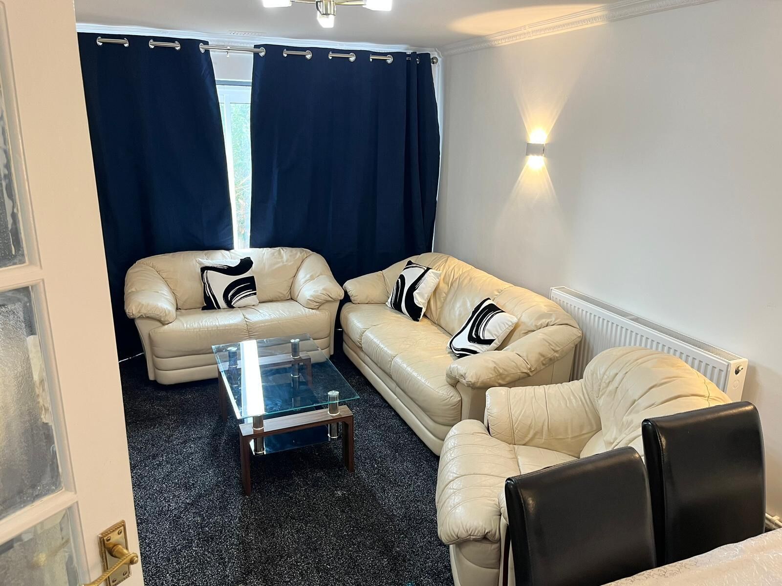 A living room with two beige leather sofas, a glass coffee table, and a black leather chair.