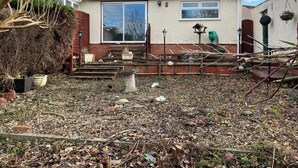 Una casa con tetto in tegole, un'ampia finestra e un giardino anteriore con dei gradini che conducono all'ingresso.