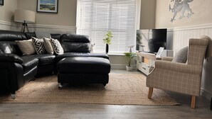 A living room with a black leather sofa, a beige armchair, a coffee table, and a TV. - 3 Bedroom Cottage in the heart of Conwy | Parking | Sleeps 4 (Conwy)