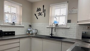 A modern kitchen with white cabinetry, a black countertop, a coffee maker, and a sign that says "Let's Eat." - 3 Bedroom Cottage in the heart of Conwy | Parking | Sleeps 4 (Conwy)