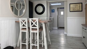 A dining area with a white wooden table and chairs, a large mirror, a wall clock, and a framed picture. - 3 Bedroom Cottage in the heart of Conwy | Parking | Sleeps 4 (Conwy)