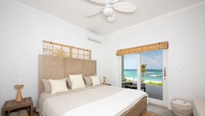 A bedroom with a large bed, a ceiling fan, a view of the ocean, and a wicker basket. - Newly Remodeled Beachfront House on Pink-Sand Double Bay Beach (Double Bay)
