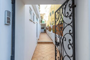 A narrow alleyway with a tiled floor, white walls, and a black wrought iron gate.
