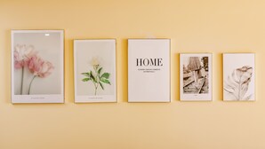 Een muur met vier ingelijste foto’s: een roze bloem, een groene plant, een zwart-wit foto van een persoon op een spoorlijn, en een veer.