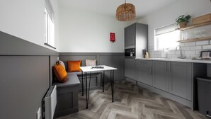 A modern kitchen with grey cabinets, a herringbone wood floor, a white dining table, and a hanging pendant light. - Goodstay Lodges by Urban Space (Barry)