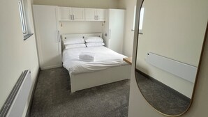 A small, neatly arranged bedroom with a single bed, a built-in wardrobe, a radiator, and a mirror on the wall. - Goodstay Lodges by Urban Space (Barry)