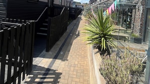 A narrow brick pathway flanked by buildings with a wooden fence on one side and a shop with colorful flags on the other. - Goodstay Lodges by Urban Space (Barry)