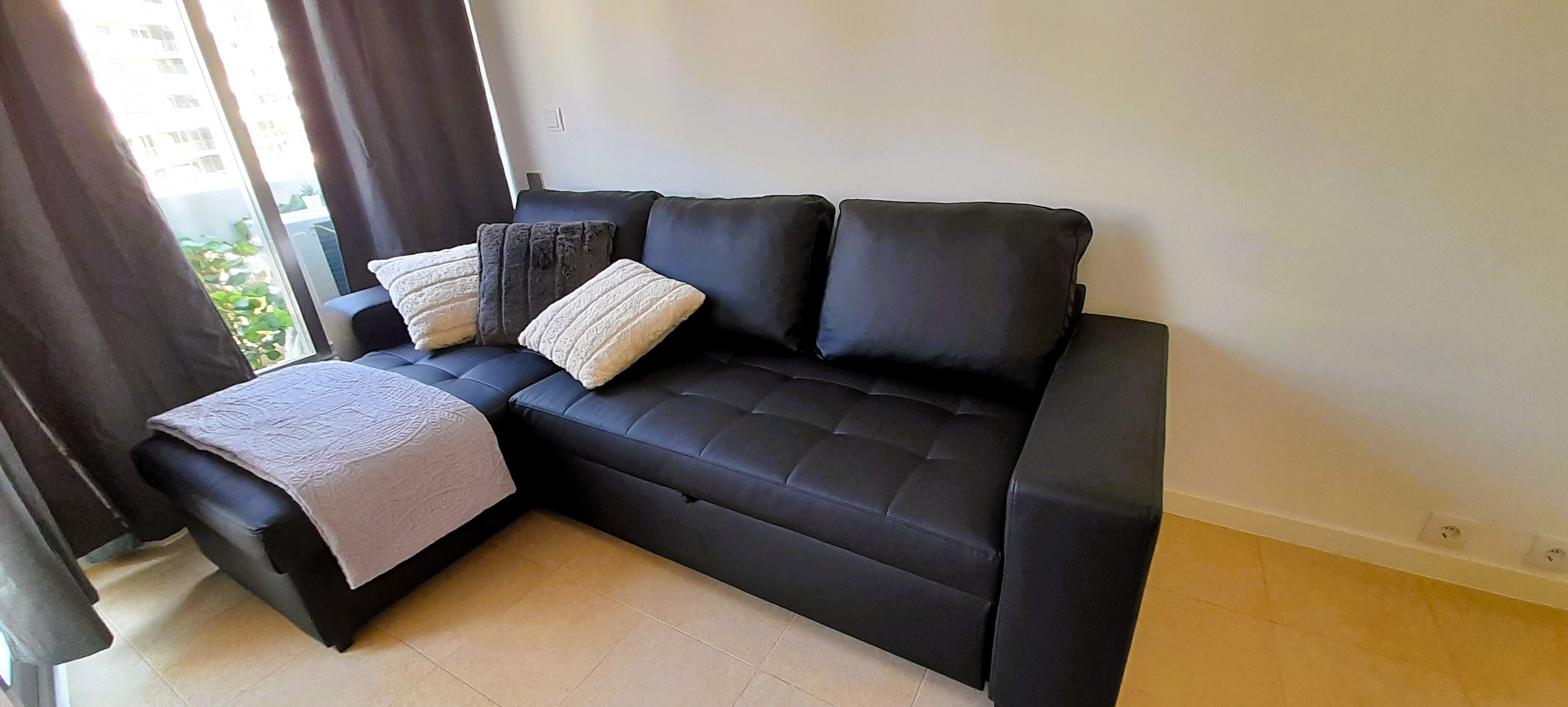 Een moderne woonkamer met een zwarte bank, een klein tafeltje en een uitzicht op het buitenleven door een raam.
