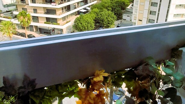 Ein Balkon mit Blick auf mehrstöckige Gebäude, einen klaren Himmel und Kübelpflanzen.