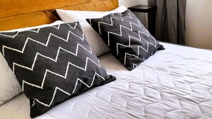 Ein Bett mit weißer Bettwäsche und zwei schwarzen Kissen mit weißen Zickzackmustern.