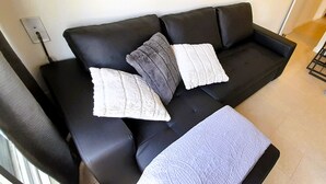 Ein schwarzes Ledersofa mit zwei weißen und einem grauen Zierkissen.