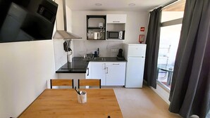 Eine kleine Küche mit Esstisch, Mikrowelle, Kühlschrank und Wand-Fernseher.