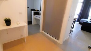 Ein Flur mit einem weißen Konsolentisch, einem Blumentopf und einer Schiebetür, die zu einem Schlafzimmer mit einem Bett und einem Nachttisch führt.