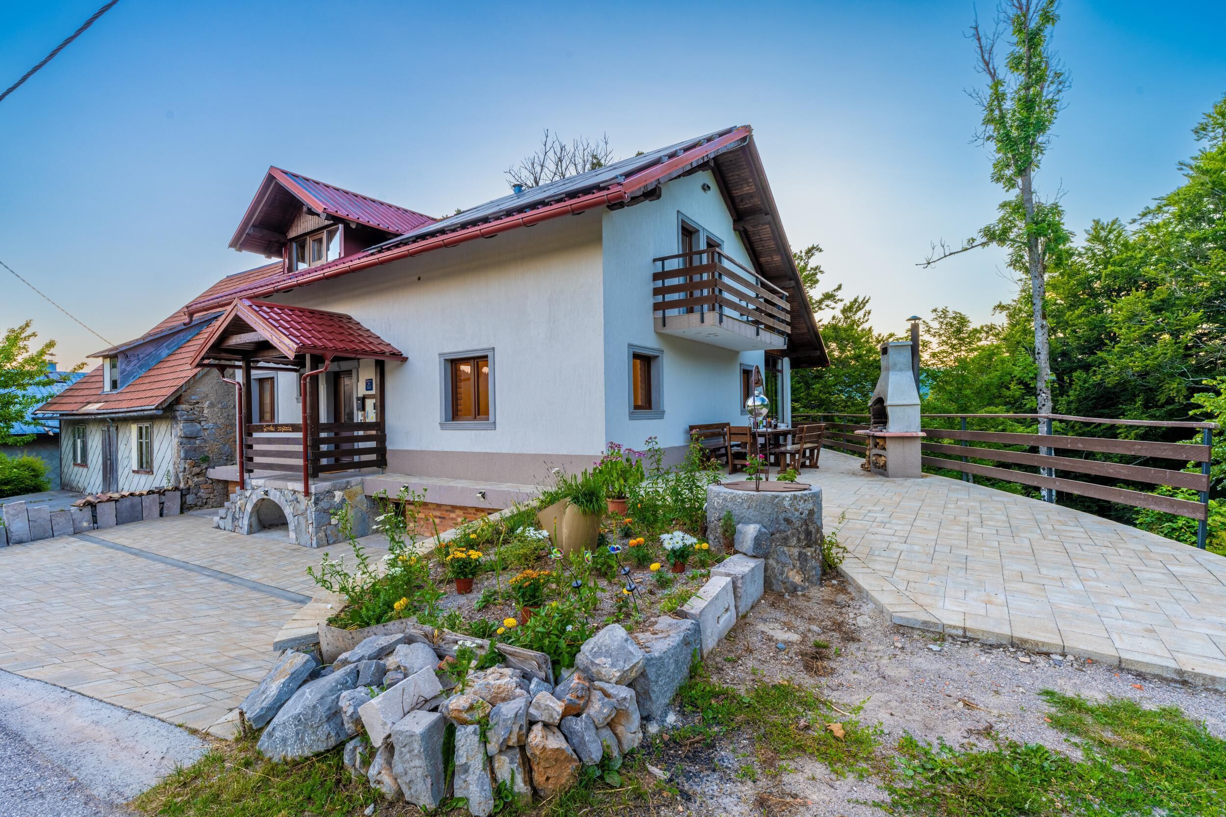 A two-story house with a sloped roof, a balcony, and a stone pathway leading to the entrance.