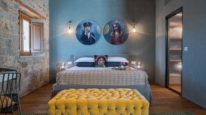 Une chambre à coucher avec un lit, un pouf jaune, un mur en pierre, une porte en bois et une fenêtre.