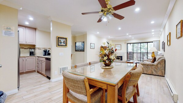 A spacious dining area with a glass-top table, wooden chairs, and a ceiling fan.