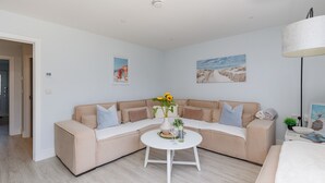 Un salon moderne avec un canapé d’angle beige, une table basse blanche et des œuvres d’art accrochées aux murs.
