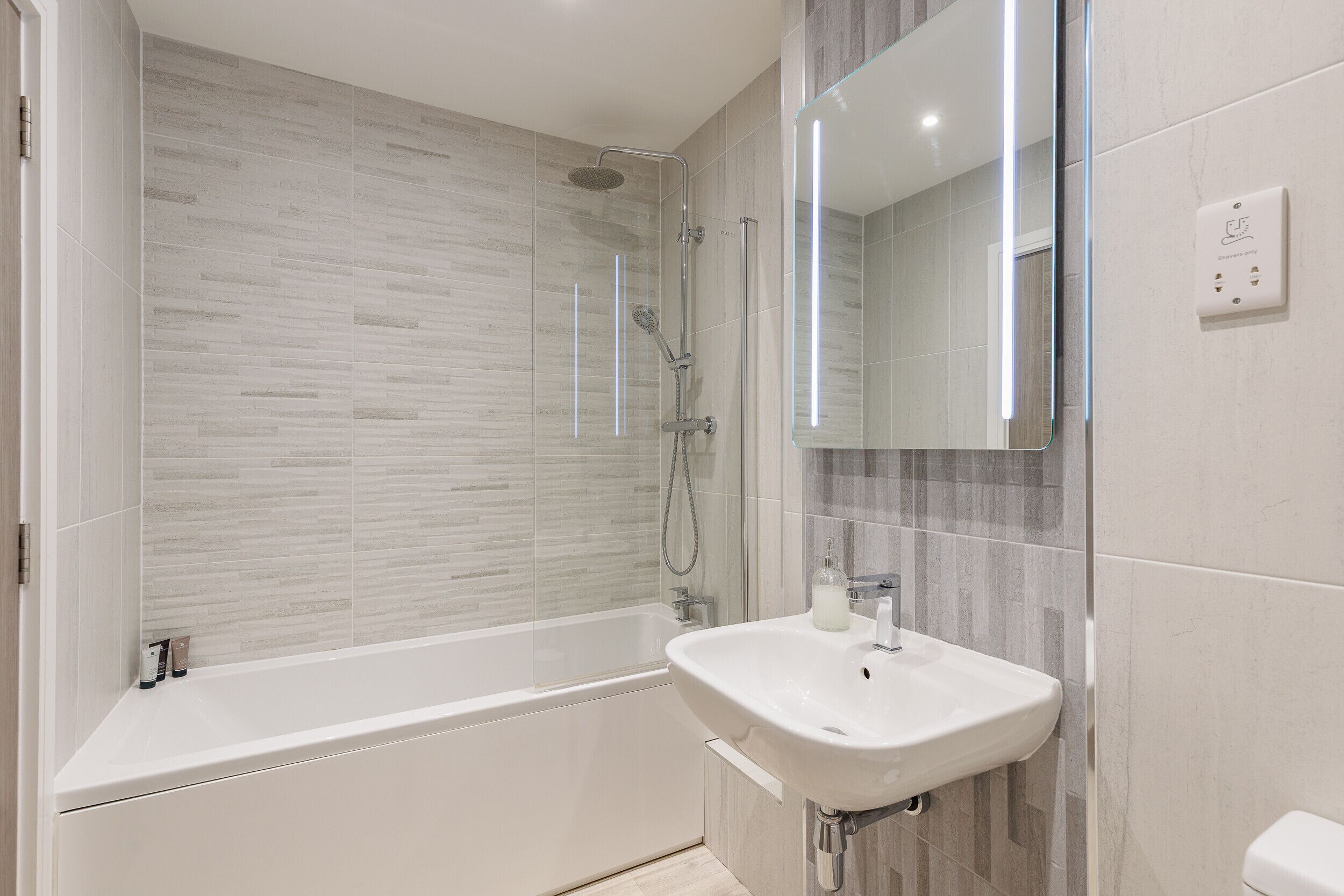Une salle de bain moderne avec une douche à parois de verre, une baignoire blanche et un lavabo surmonté d’un miroir.