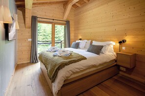 A wooden cabin bedroom with a large bed, a nightstand, and a window with curtains. - Ski Chalet Bonnabelle, Hot tub, garden, parking (Chamonix)