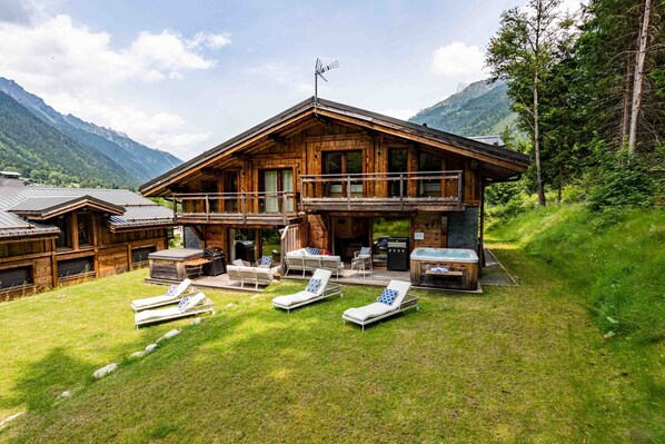 A wooden chalet with a balcony, outdoor seating, and a hot tub.