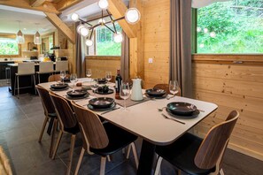 Un comedor con una larga mesa dispuesta para seis personas, sillas de madera y una cocina al fondo.