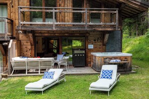 Una cabaña de madera con balcón, mobiliario exterior, una parrilla de barbacoa y un jacuzzi.