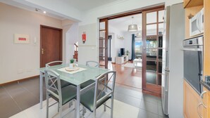 Een moderne keuken met roestvrijstalen apparatuur, een glazen eettafel en een schuifpui naar een balkon.
