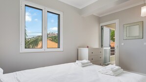 Een slaapkamer met een bed, een dressoir, een spiegel en een raam met uitzicht op palmbomen en gebouwen.