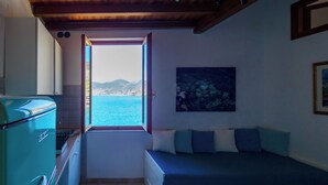 Una stanza accogliente con un letto, una finestra vista mare, angolo cottura e soffitto a travi in legno.