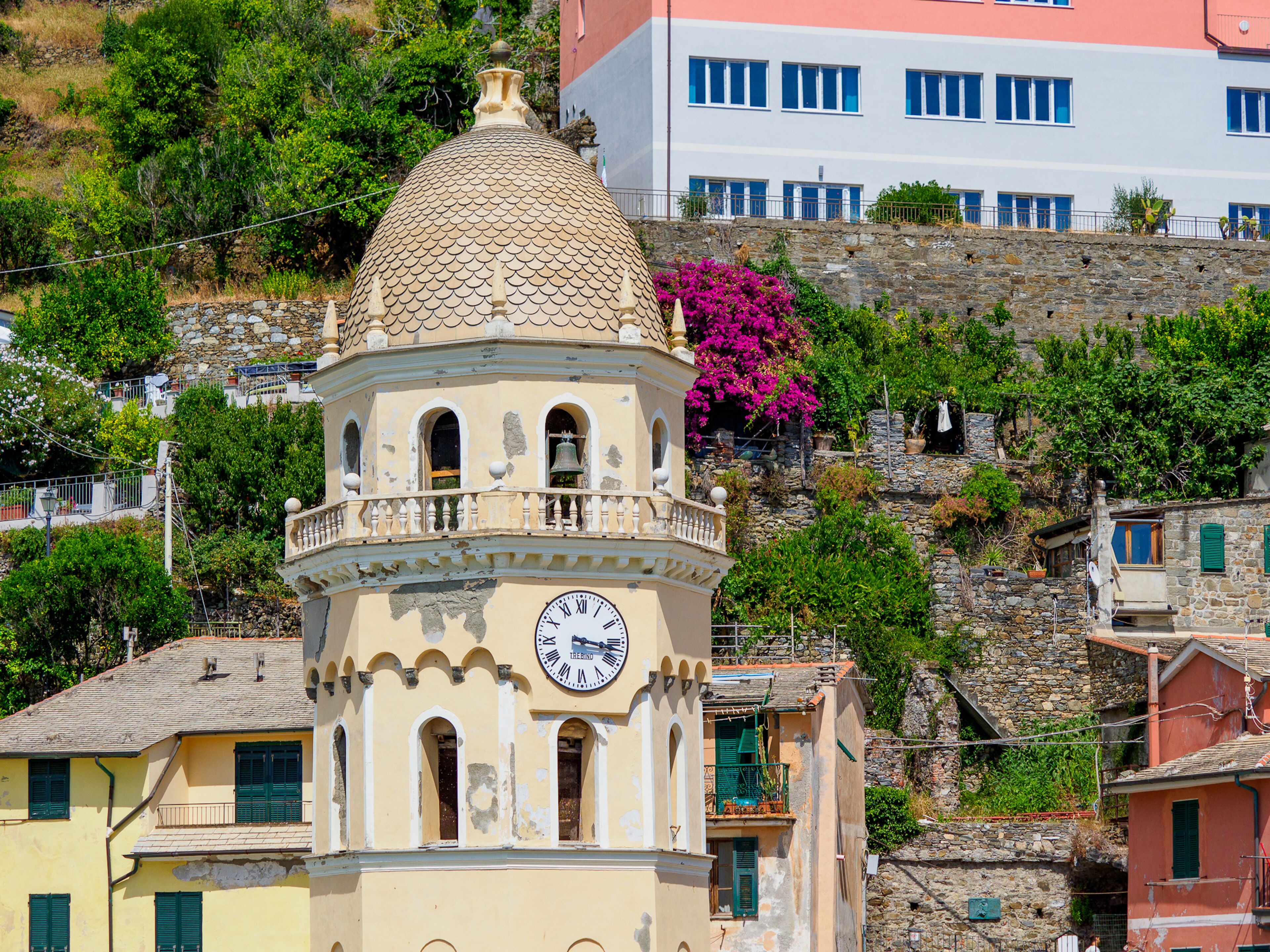 A historic building with a clock tower, stone walls, and a hillside backdrop.