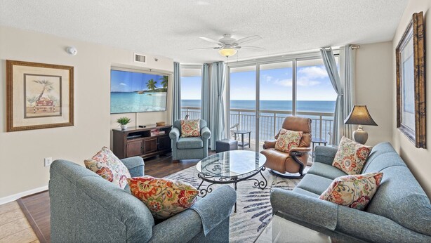 A spacious living room with a large TV, comfortable seating, a ceiling fan, and a view of the ocean. - Oceanfront Crescent Beach 1K 2Q - Crescent Shores - 1609 (North Myrtle Beach)