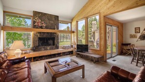 Ein gemütliches Wohnzimmer mit Kamin, Ledersofas, einem Couchtisch und großen Fenstern mit Blick ins Freie.