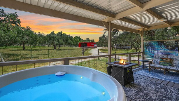 A covered outdoor area with a hot tub, seating, and a view of a sunset. - Windmill Ranch- Glamping Star RV  I Hot tub, stargazing (Wimberley)