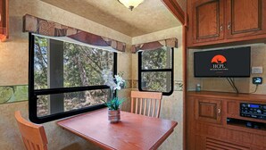 A compact kitchen with wooden cabinets, a built-in TV, and a window with curtains. - Windmill Ranch- Glamping Star RV  I Hot tub, stargazing (Wimberley)