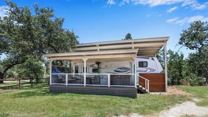 A small, single-story RV with a covered porch and a "RAPTOR" logo. - Windmill Ranch- Glamping Star RV  I Hot tub, stargazing (Wimberley)