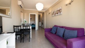 A living room with a purple sofa, a dining table with chairs, a TV, and a ceiling light.