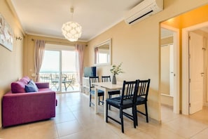 A living area with a sofa, dining table, chairs, a TV, and a balcony with curtains.