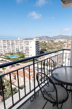 A balcony with a table and chairs, overlooking a residential area with a pool and buildings.