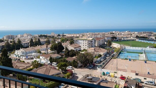 A coastal cityscape with residential buildings, a sports field, and a clear view of the sea.