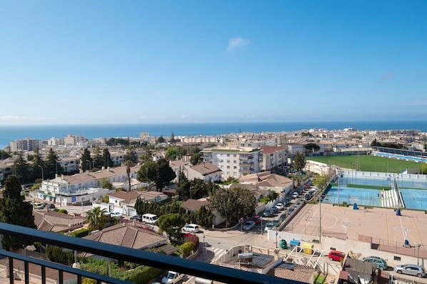A coastal cityscape with residential buildings, a sports field, and a clear view of the sea.