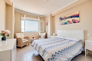 A bedroom with a bed, a window, a chair, a small table, and a painting on the wall.