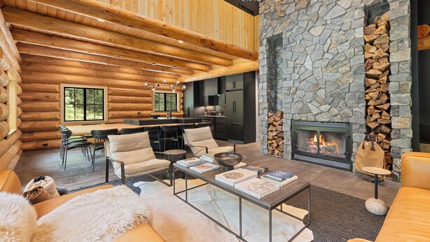 L’intérieur d’une cabane en rondins, avec une cheminée en pierre, des poutres en bois au plafond et un coin repas.