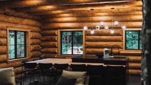 L’intérieur d’une cabane en rondins comprend un coin repas avec des chaises, une table et une fenêtre donnant sur la forêt.