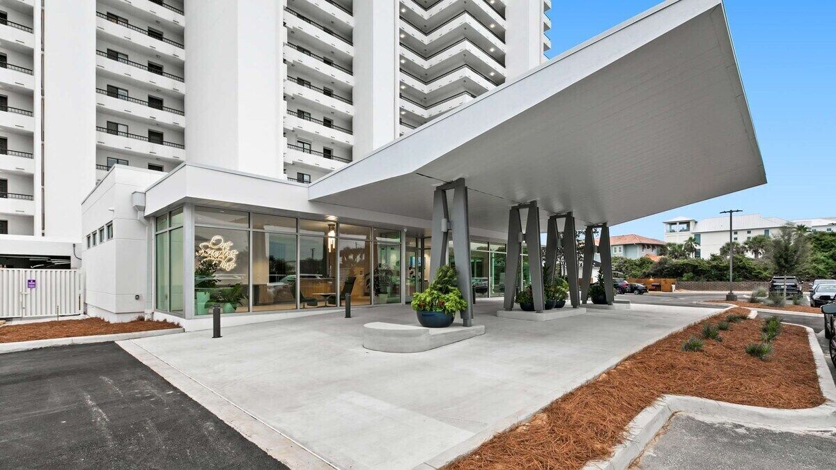 En modern hotellentrél med en överbyggd gångväg, glasdörrar och en parkeringsplats.