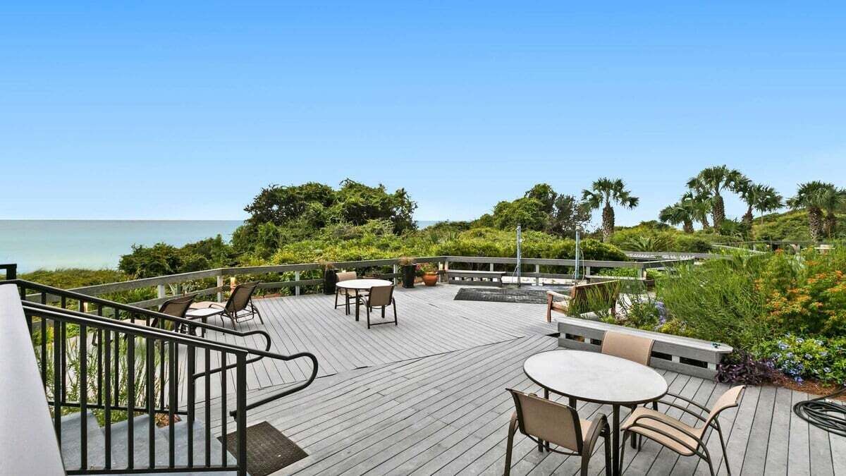 A wooden deck with outdoor seating, overlooking a beach and palm trees.