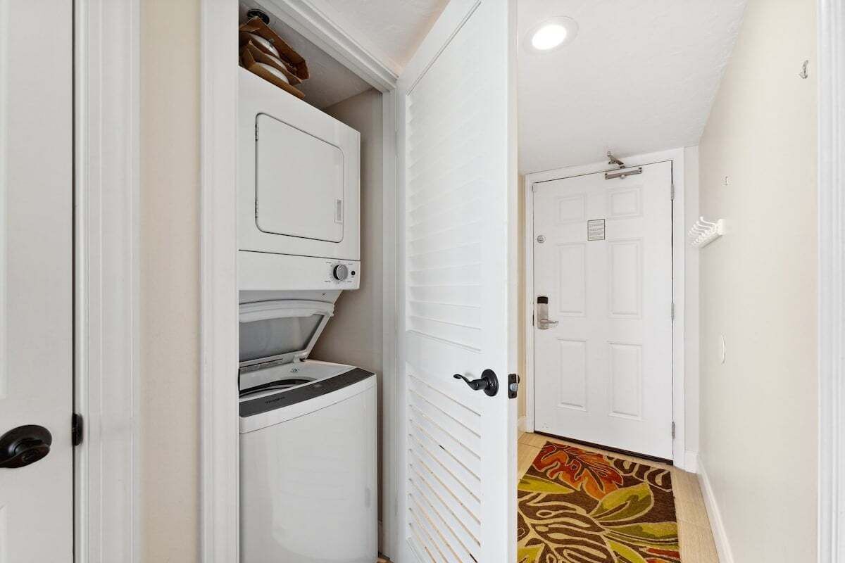 A laundry room with a washer and dryer, a door with a handle, and a patterned carpet.