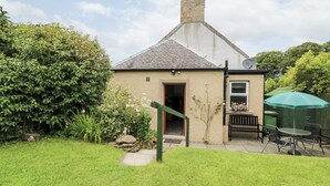 A small house with a sloped roof, a chimney, and a door leading to a porch. - Katmoget Cottage (Cupar)