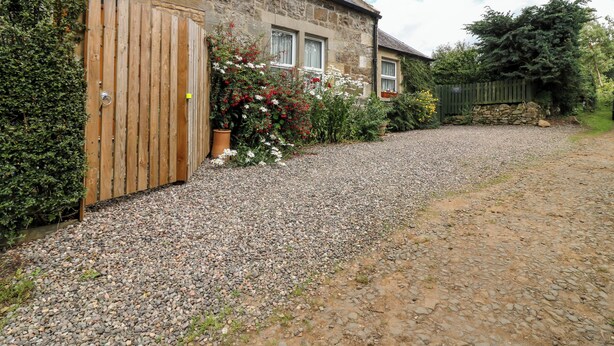 A stone house with a gravel driveway and a wooden gate. - Katmoget Cottage (Cupar)